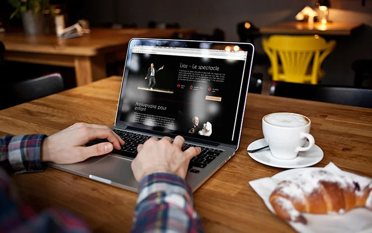 Man visiting Lioz Website on his laptop in a cafe with a coffee and a croissant