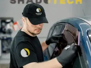 Technicien ShadoTech appliquant un film teinté sur une vitre de voiture dans l’atelier